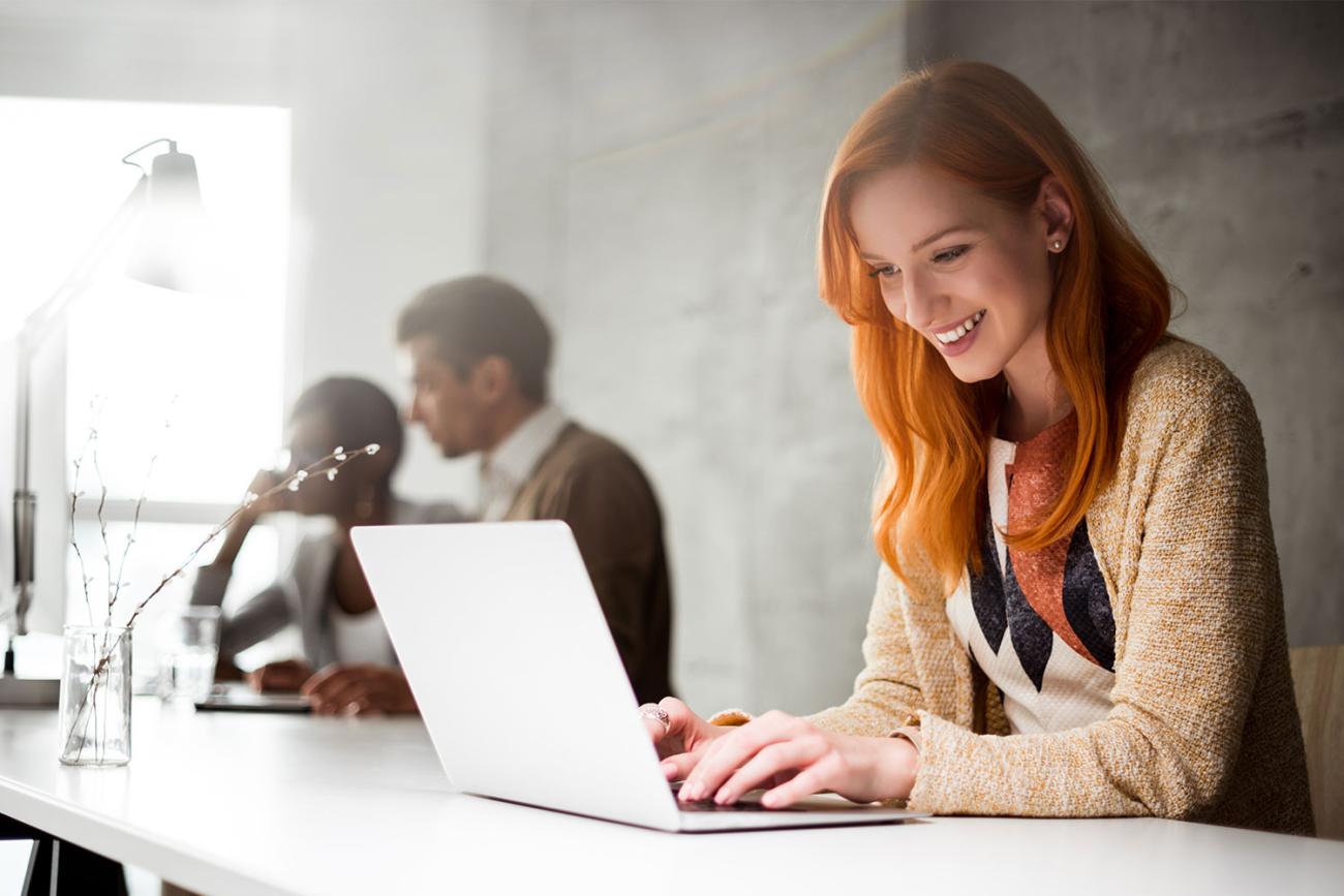 Woman with red hair smiling down at laptop screen in front of her