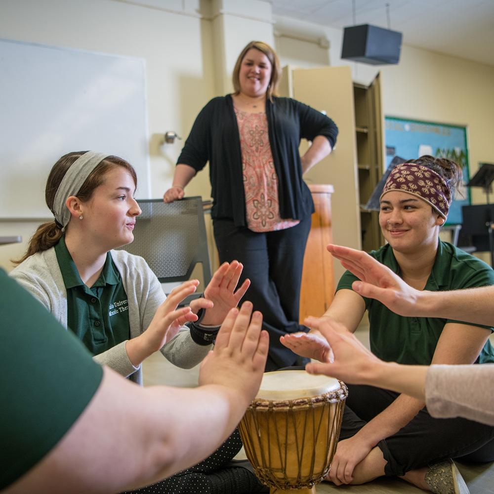 Students sit in a circle playing a bongo together.