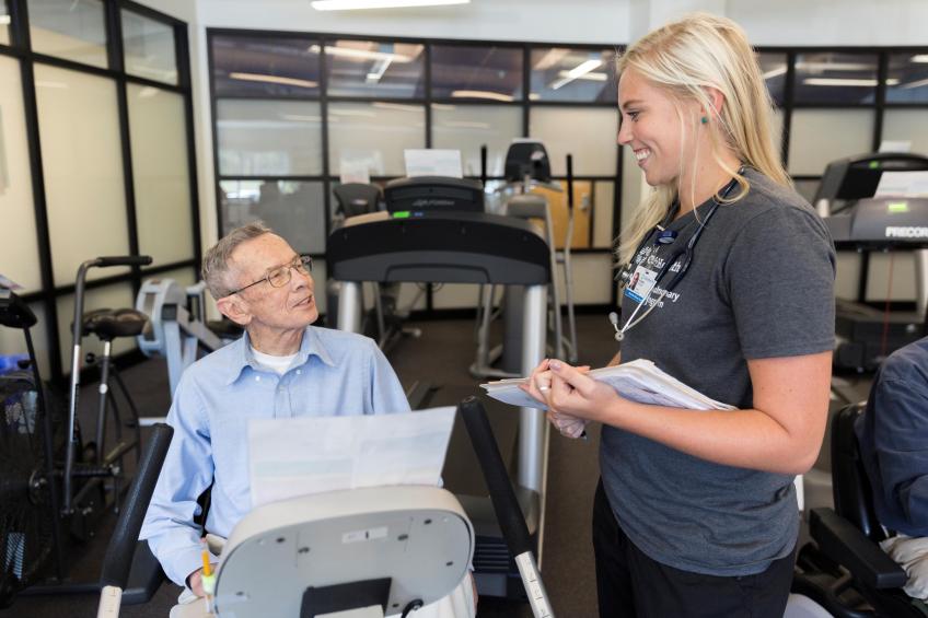 Female practitioner speaking with  man on exercise bike 