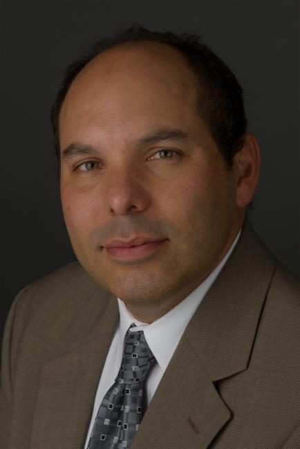 Headshot of Donald Brown wearing a tan suit jacket and white shirt with a tie.