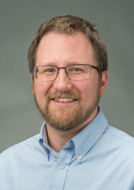 Headshot of a smiling Mathew Felton-Koestler wearing a blue dress shirt