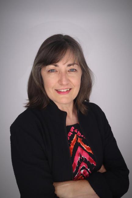 Headshot of Anita Simpson wearing a black jacket and pink and purple top with her arms folded.