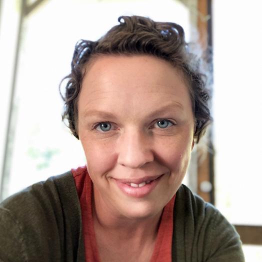 Headshot of a smiling Amy Wolfe wearing a dark jacket and orange top.