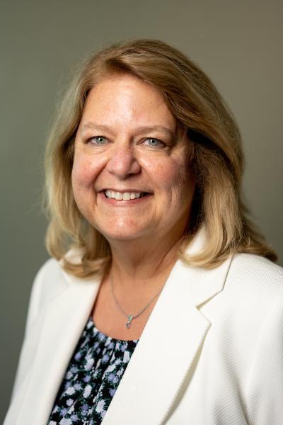 Headshot of a smiling Lorna Buskirk wearing a white suite jacket and a dark print top.