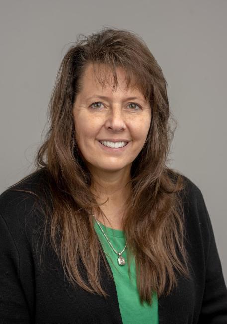 Headshot of a smiling Monica Price wearing a black jacket and green top.