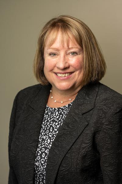 Headshot of a  smiling Karen Corcoran in a dark suit jacket and print blouse 