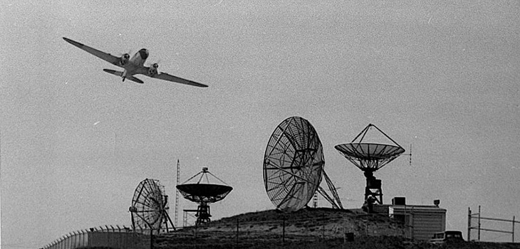 black and white image of a plane flying over telecommunications equipment
