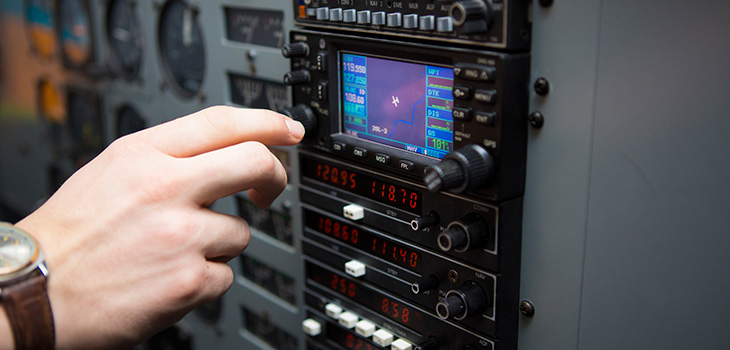 Hand reaching toward a control panel with a small screen showing an airplane's position