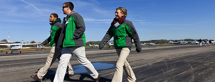 Three young adults in matching jackets walking down an airport runway