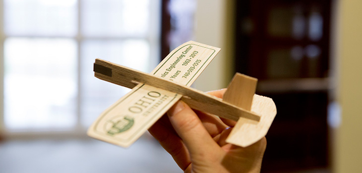 Hand holding toy balsa wood airplane with Ohio University logo on the wing