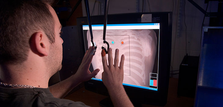 Person using a human-computer interface where their index fingers control rods descending from above, in front of a computer screen showing human ribs with superimposed dots and lines