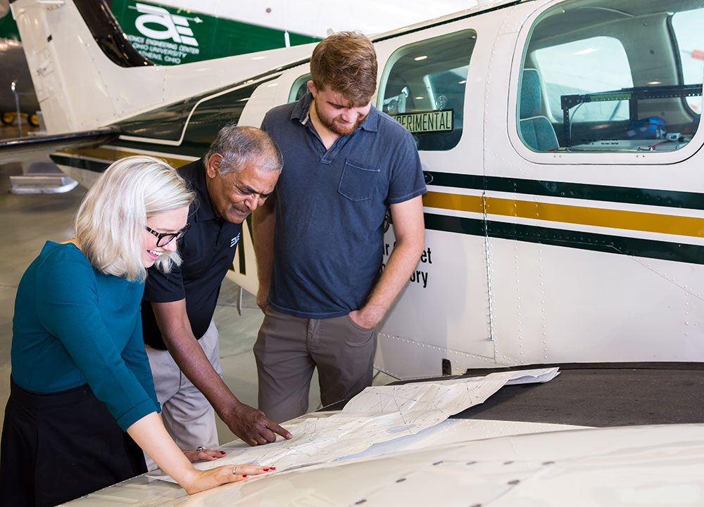 Three researchers, one female and two males, look over plans in an airport hangar