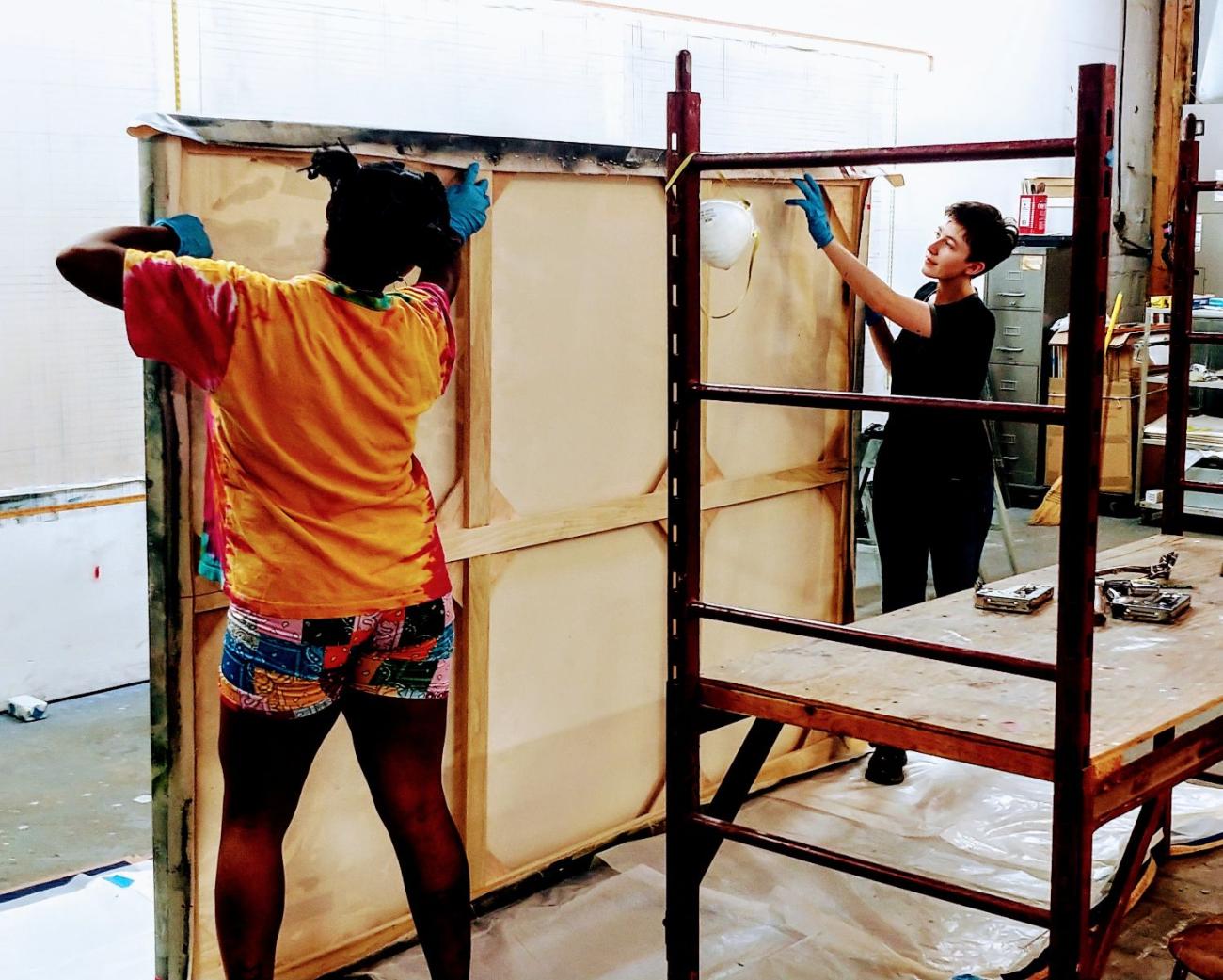 Students handle large painting with scaffolding in studio