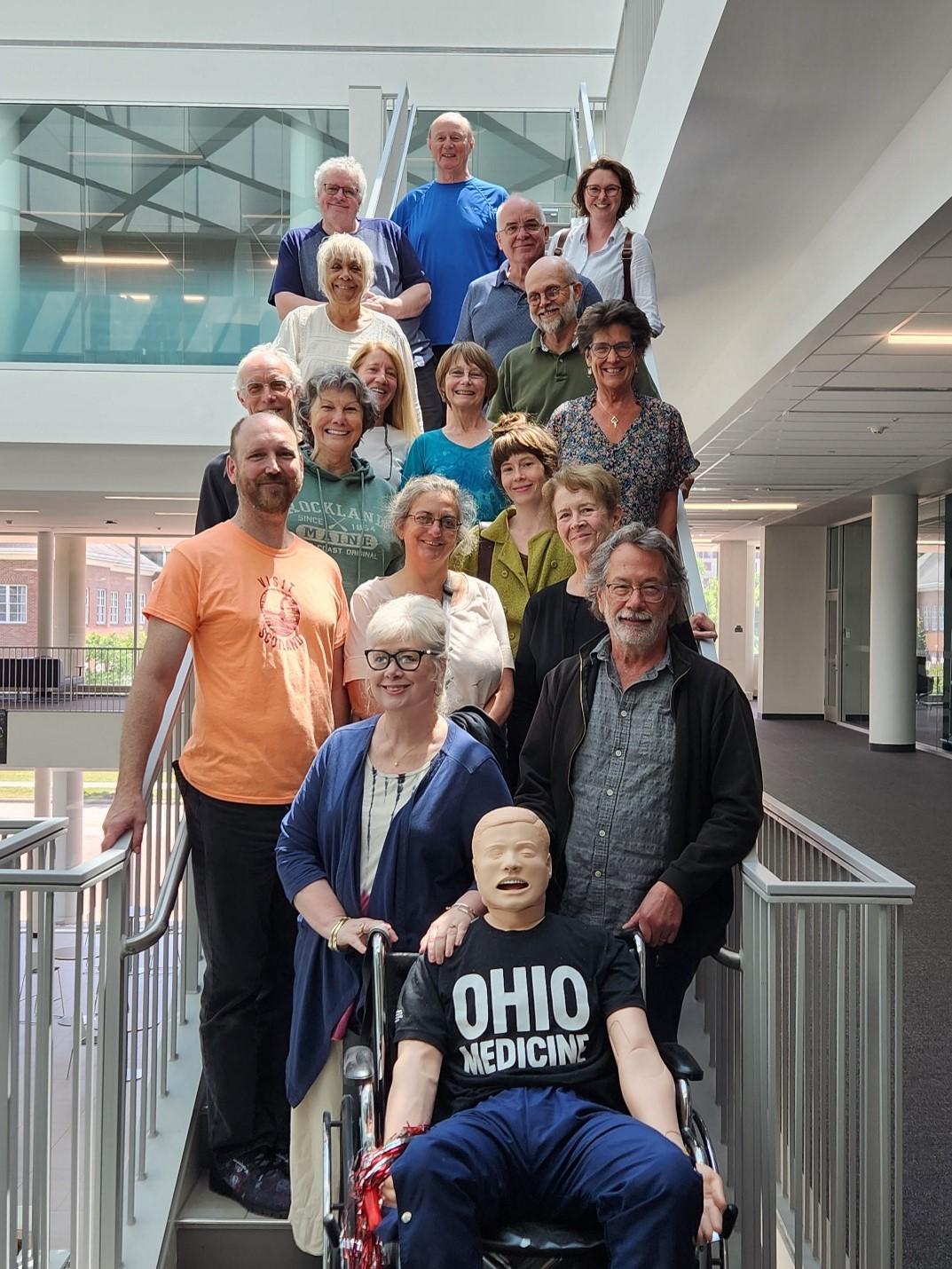 A group of 17 standardized patients pose on a stairway in Heritage Hall