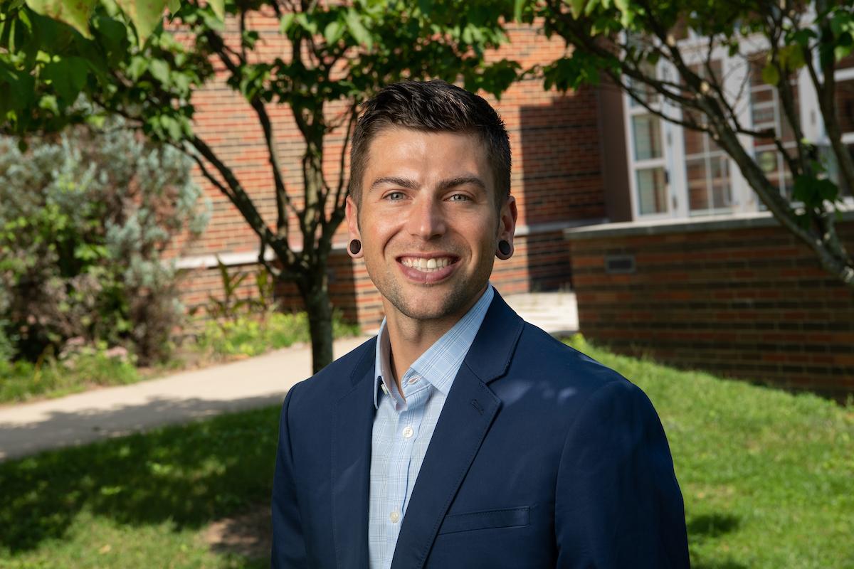 Cory Baumann portrait with trees, grass and brick building in background