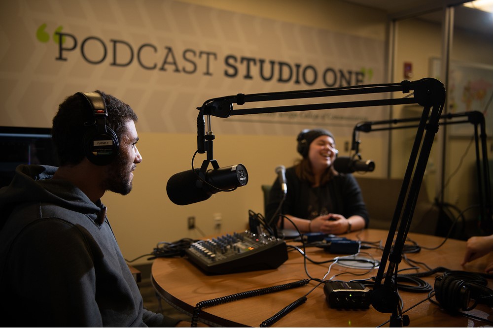 Two students in a podcasting studio with microphones and recording equipment around them