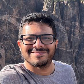 Veeren Naidu Poola smiling while taking a selfie while wearing a gray shirt and black-framed glasses