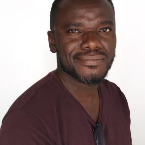 Andrew Ekuban smiling at the camera with a raised brow and glasses clipped to his burgundy shirt