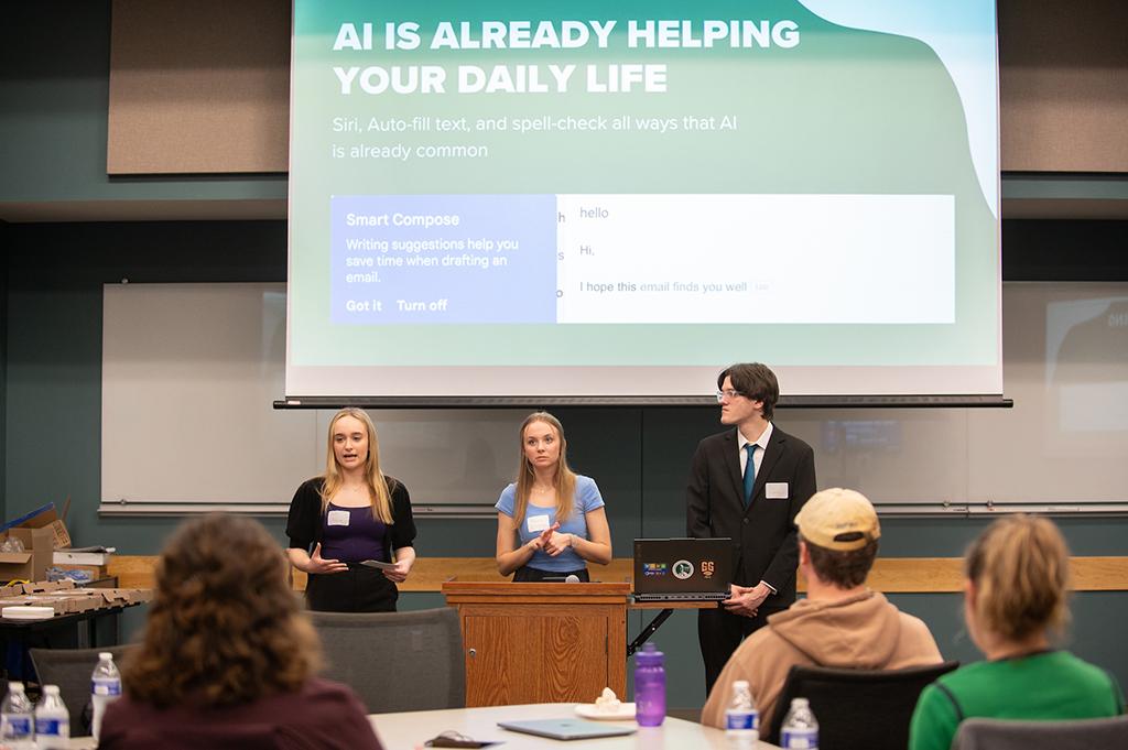 3 students giving a powerpoint presentation to audience members on AI