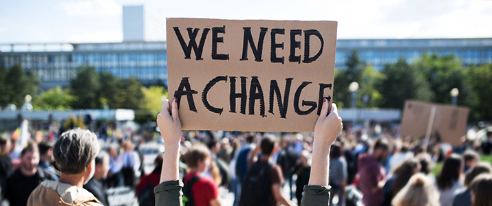Hands hold a sign during a protest that says "we need a change"