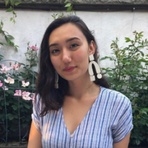 Ami Scherson in a vertically striped blue and white t shirt, posed in front of a small garden and white wall.