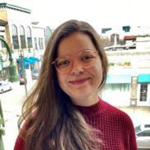 Faith Ryon smiles at the camera, wearing glasses and a dark red sweater.