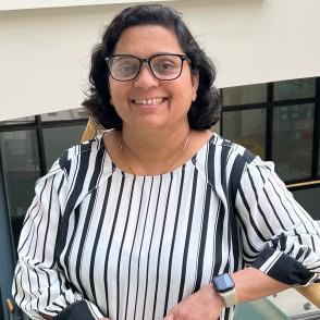 Rita Sharma in a vertically black and white striped shirt with one arm propped up and leaning on it.