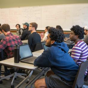 A classroom full of students, sitting at desks, looking at the front of the class