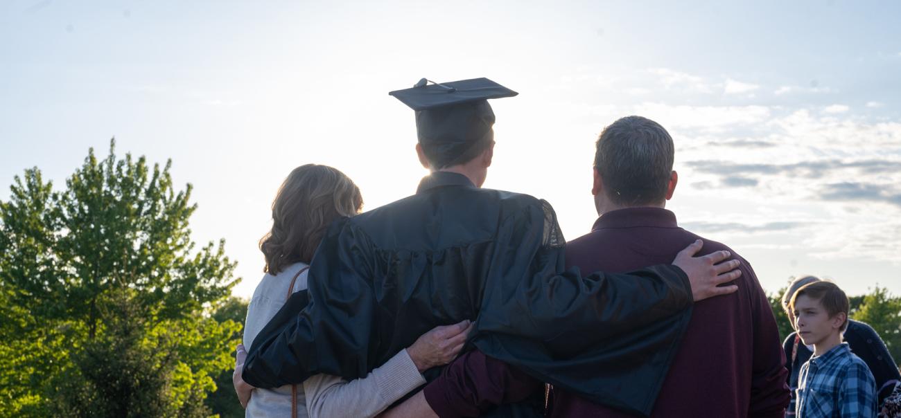An Ohio University student poses wearing their cap and gown, with their parents by their side