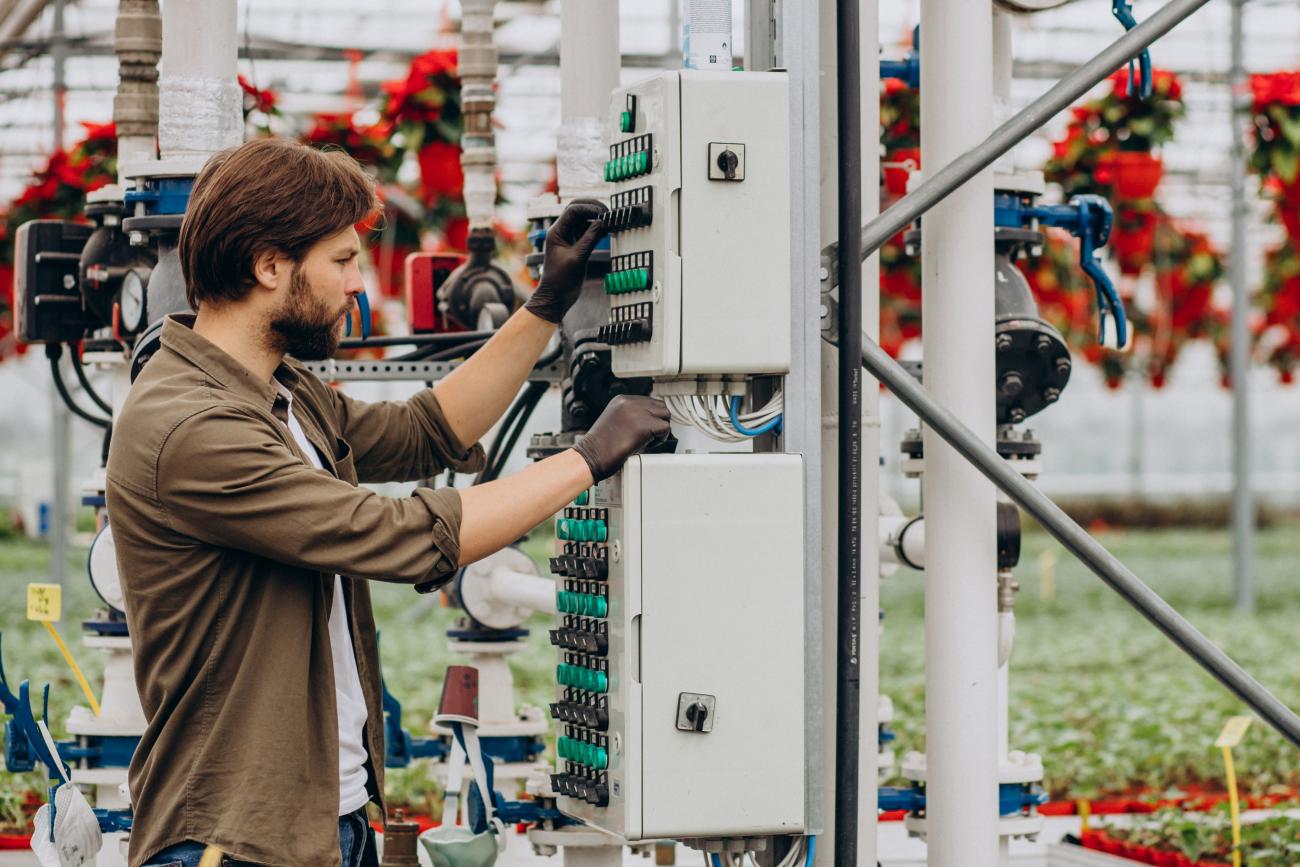 An electrical engineer works In a greenhouse, fixing an electrical sprinkling system. Image by senivpetro on Freepik.