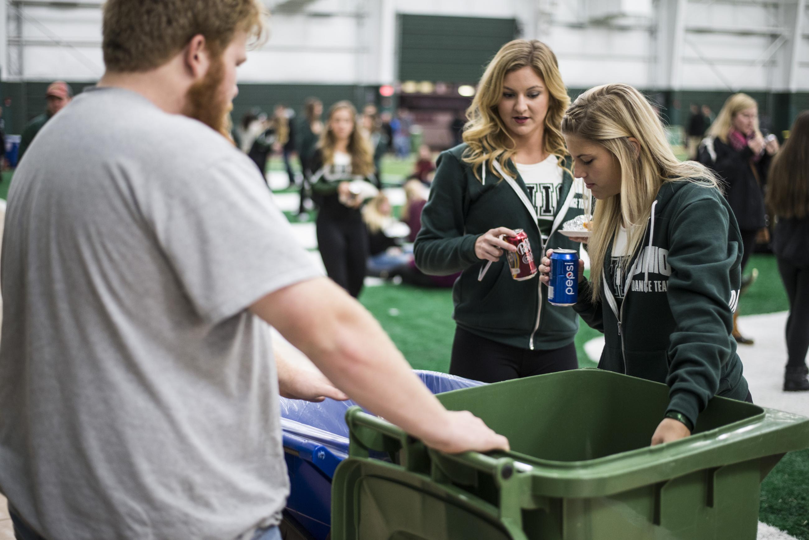 two girls putting cans into a recycling bin