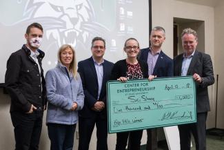 a group of people stand with a giant check made out to Sci Share for $1000