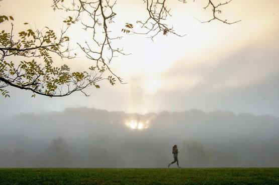 A person runs on the Athens bike path with a sunset peeking through the clouds in the background