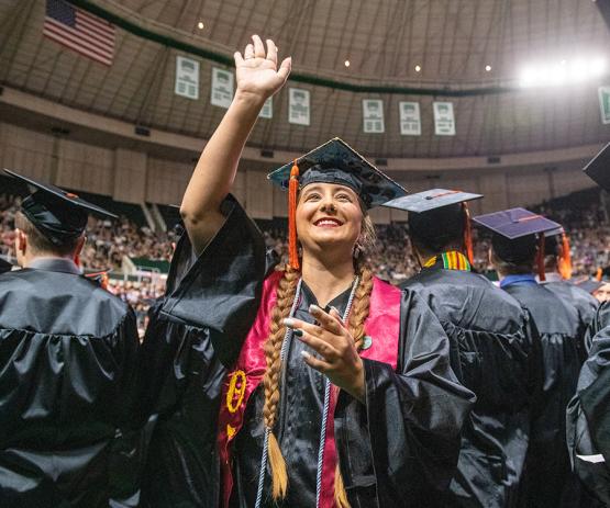 Undergraduate student smiles and waves to their family during Commencement