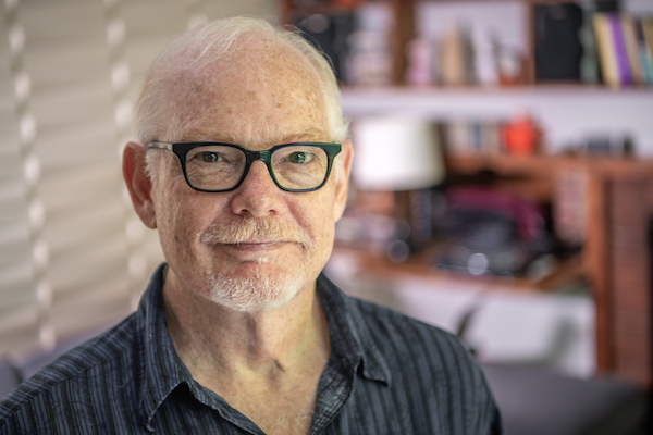 A man in black glasses smiles at the camera