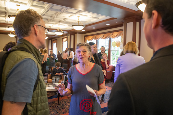 Three people stand in a group at a party, talking animatedly