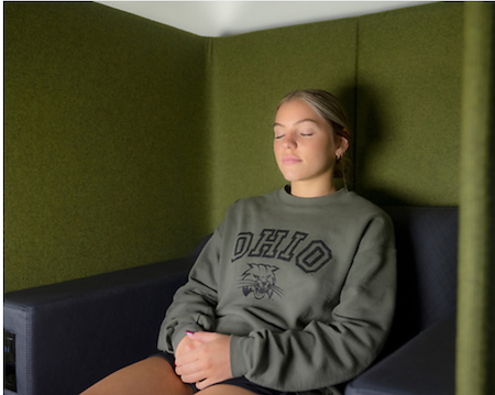 A student wearing an OHIO sweatshirt meditates with closed eyes in an enclosed, serene space