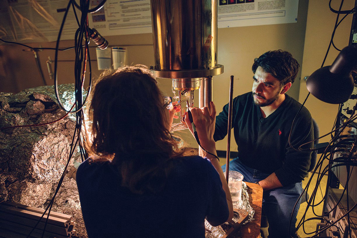 a male and female graduate student work on complex lab equipment with tweezers