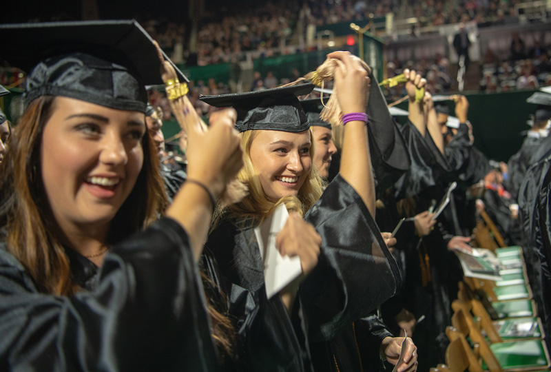 Kristine N. Pollard (left) and Carly Joy Pavey (center) move their tassels from right to left at Fall Commencement. 