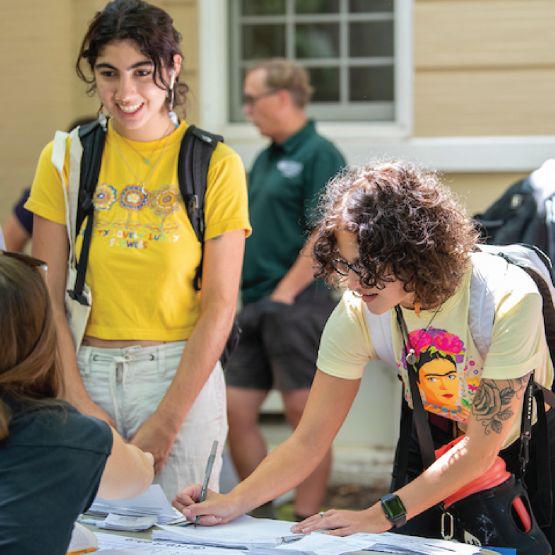 OHIO students are shown at a table signing papers and talking