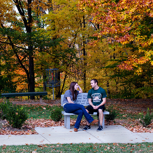 Two students sit on a bench and talk.