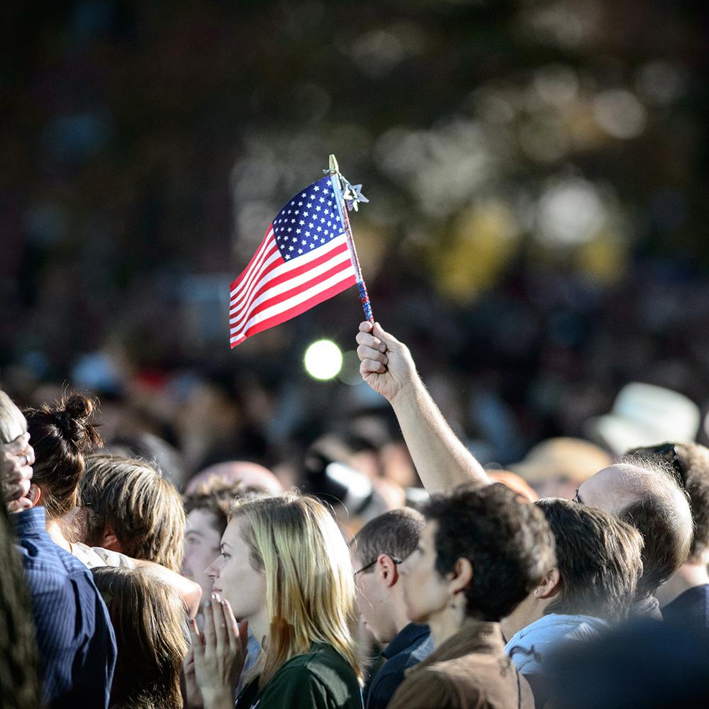 A person holds up a flag in a sea of people.