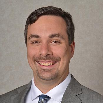 Michael Nav Headshot - smiling man with short brown hair and goatee, suit and tie