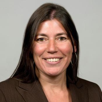 Headshot of smiling woman with long, dark hair and dark suit jacket. 