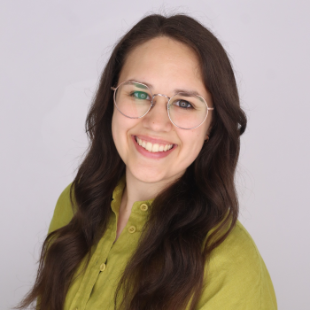 Smiling woman with long dark hair, glasses and green shirt with a light background 