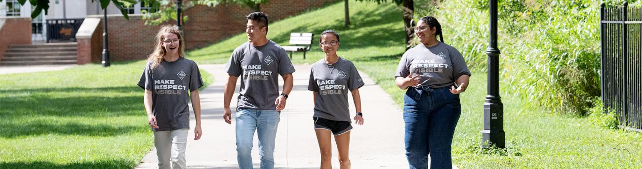 Four students wearing Make Respect Visible t-shirts talk as they walk across campus.