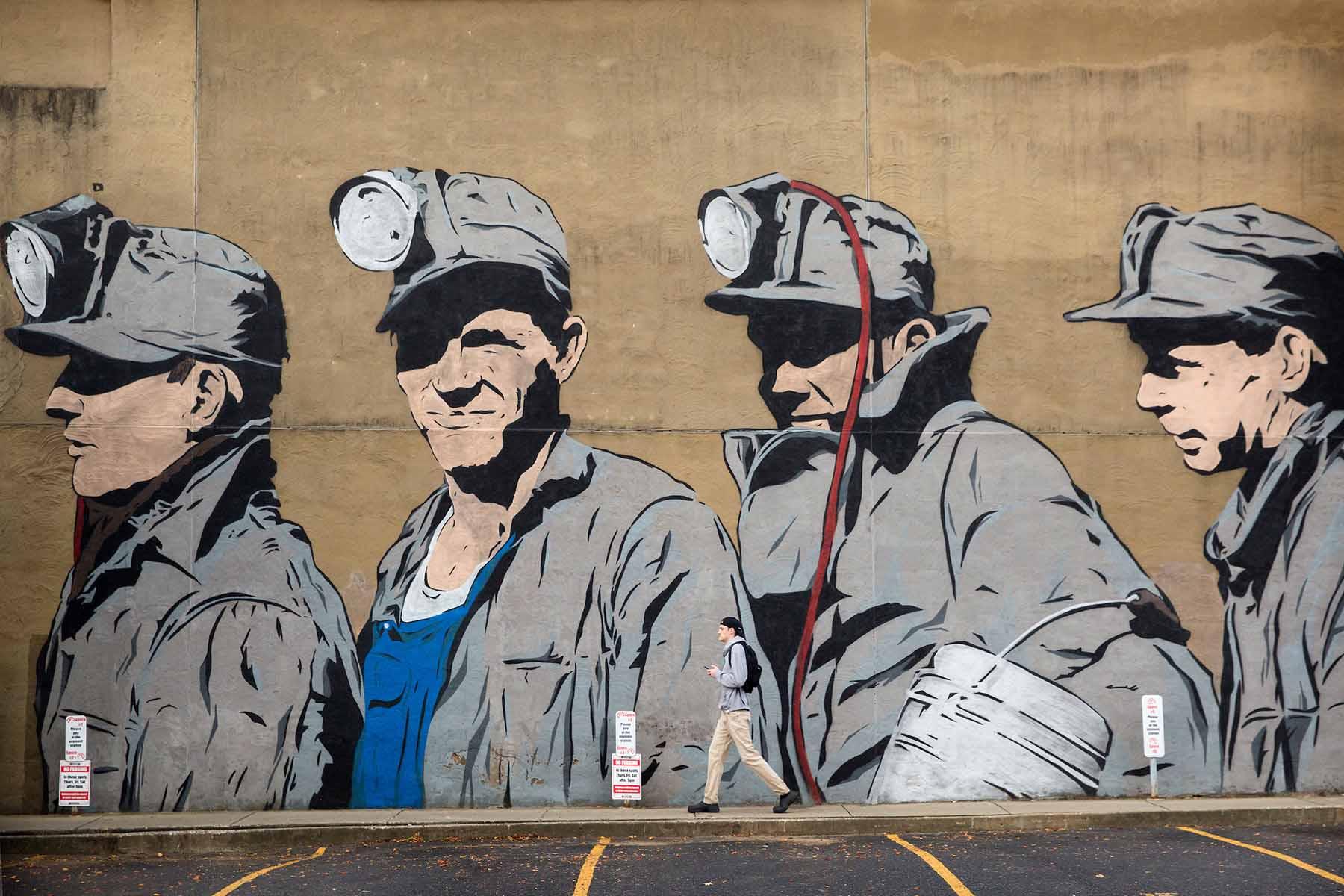 Photograph of a pedestrian passing ther coal mine mural in Uptown district or Athens, Ohio on Oct. 27, 2016. The mural was created by Chris Stain with the help of Ohio University Fine Arts students