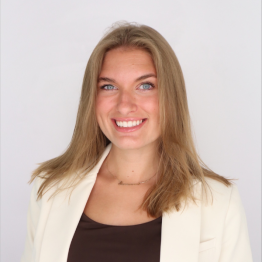 Savannah Dawson smiling in front of a white photo background with a brown shirt and white blazer. 