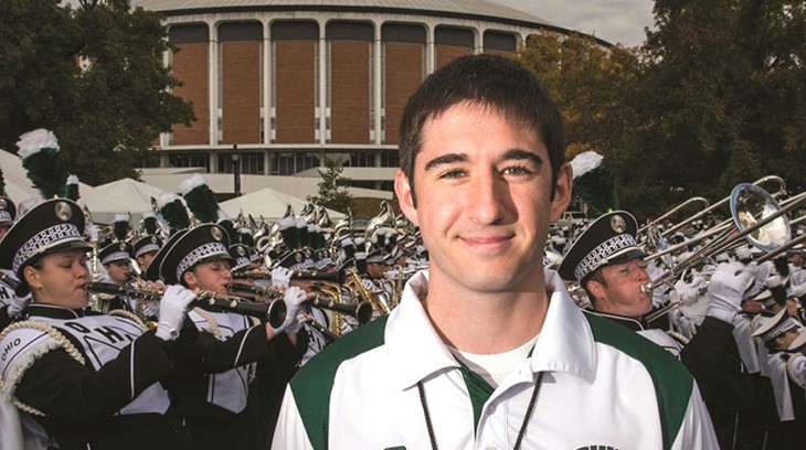 Student stands in front of the Convocation Center and the Marching 110, Ohio University's marching band