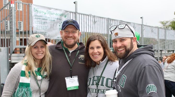 Four Ohio University alumni pose for a picture, all wearing OHIO gear